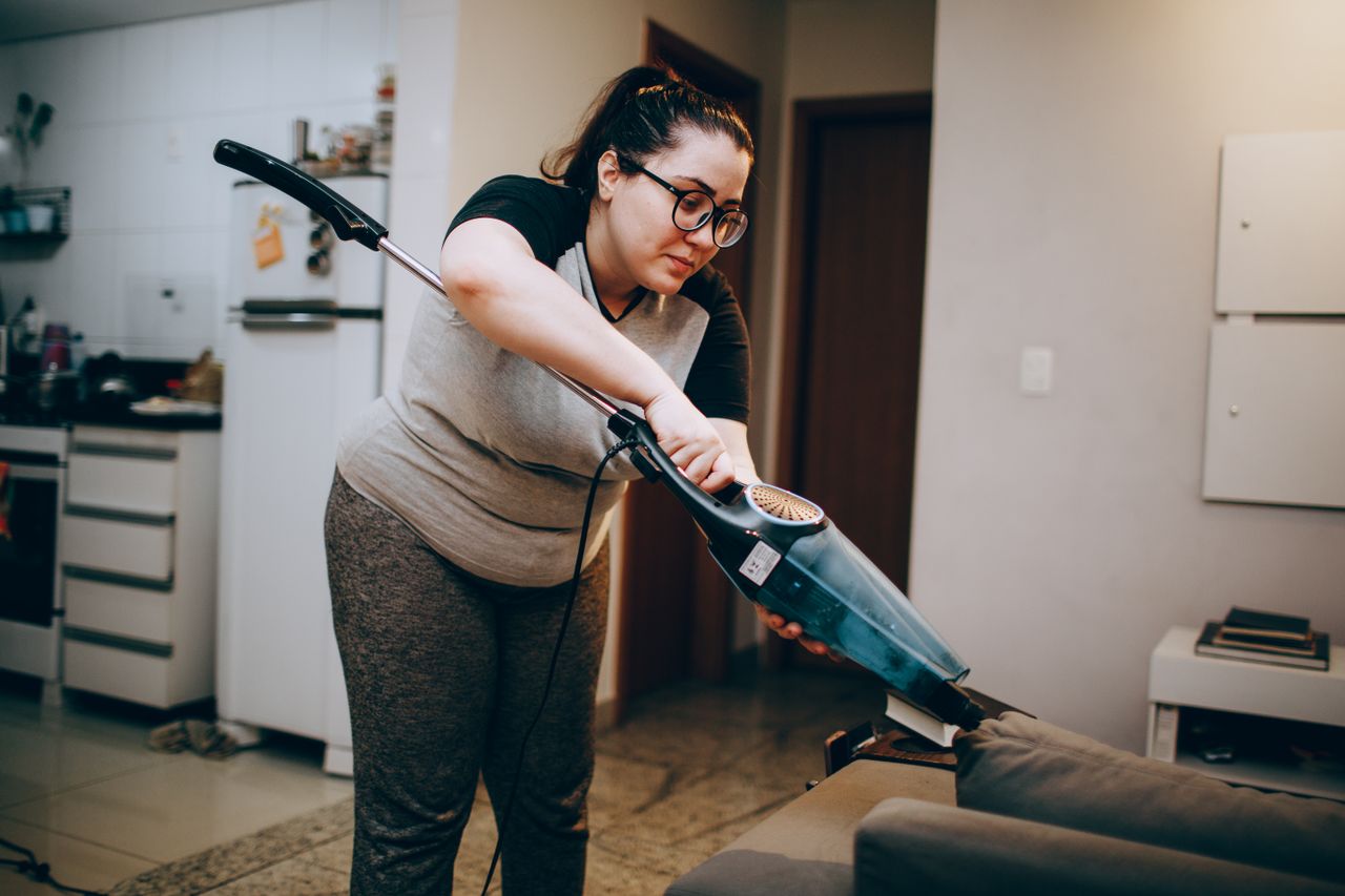services-01 A woman vacuuming a couch in a cozy living room setting, emphasizing daily housework.